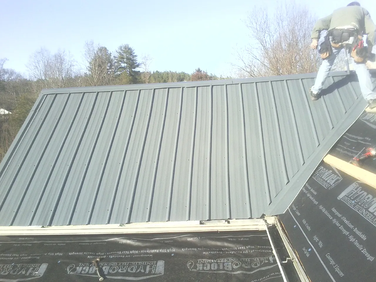 Crew installing dark green standing seam panels over synthetic underlayment in Greenville