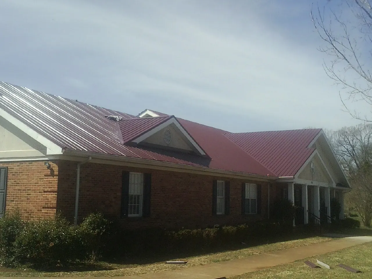 Red metal roof with gabled entries on a long brick building, from a Hail Damage Roof Repair job in Greenville